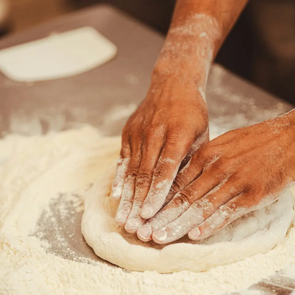 Des mains farinées aplatissent une pâte à pizza.